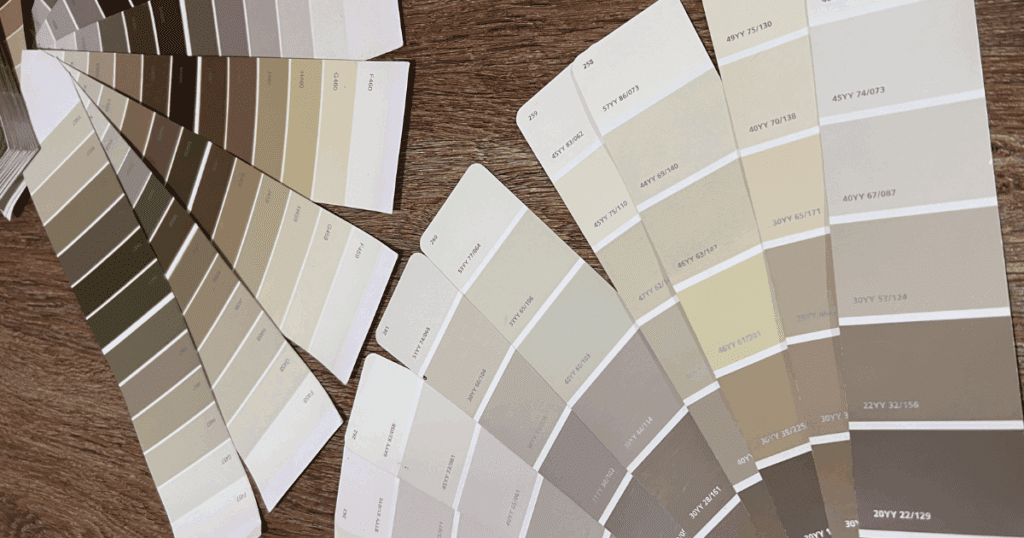 A selection of neutral-toned paint swatches in beige, taupe, and greige hues arranged across a wood surface, showcasing a variety of interior paint options.
