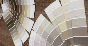 A selection of neutral-toned paint swatches in beige, taupe, and greige hues arranged across a wood surface, showcasing a variety of interior paint options.