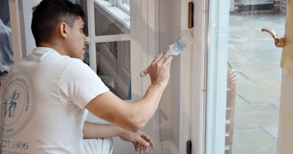 Close-up of a professional A.G. Williams painter carefully applying white paint to a door frame with a precision brush, showcasing painting contractor tips in action.