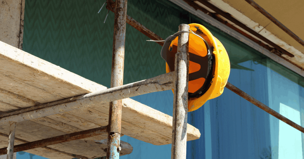 Yellow safety helmet hanging from a weathered scaffold at a commercial building site.