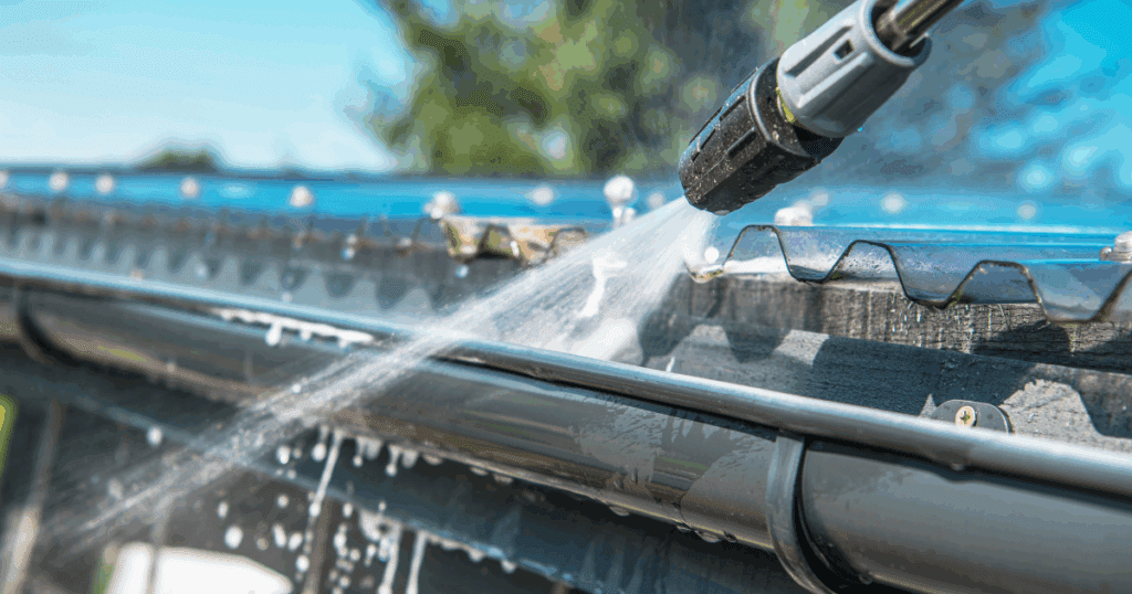 Power washing a gutter to maintain clean gutters and improve exterior appearance and drainage efficiency.