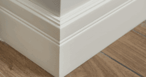 Detailed view of crisp, cleanly painted baseboards at a corner joint over hardwood flooring.