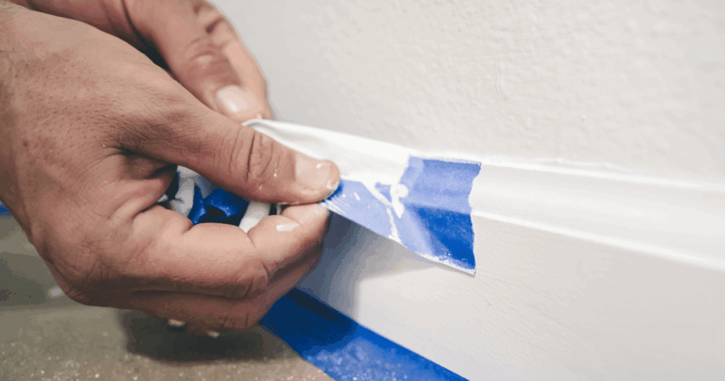 Close-up of a professional carefully removing painter’s tape from a freshly painted baseboard.
