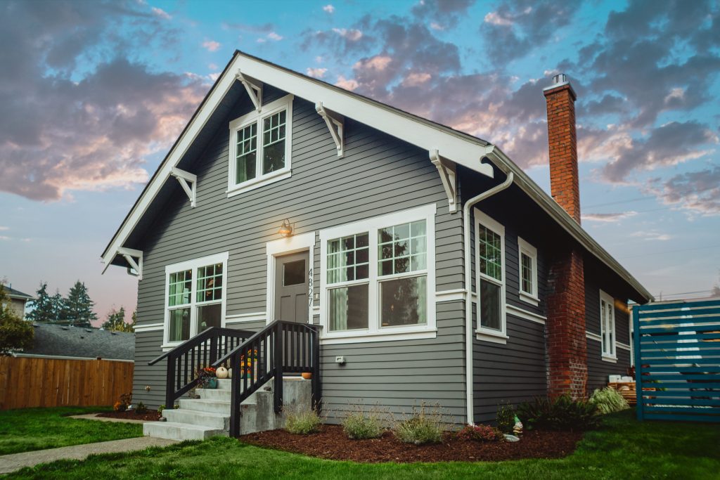 Grey house with white trim. Sky is darkening as if it is evening