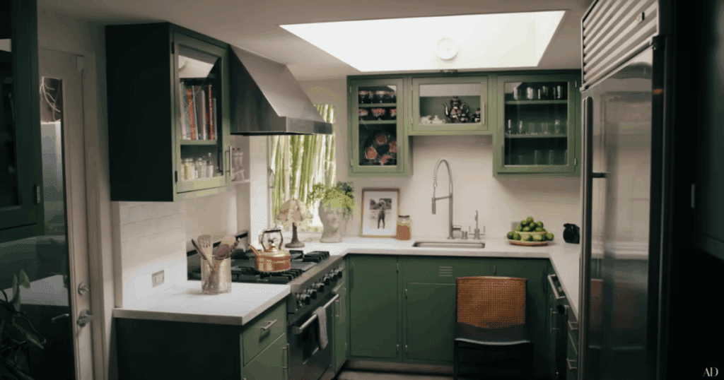 A cozy green kitchen with glass-front cabinets and copper accents, bathed in natural light from a skylight.
