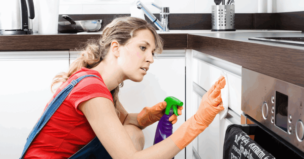 Woman cleaning kitchen cabinets as part of painted cabinet maintenance.