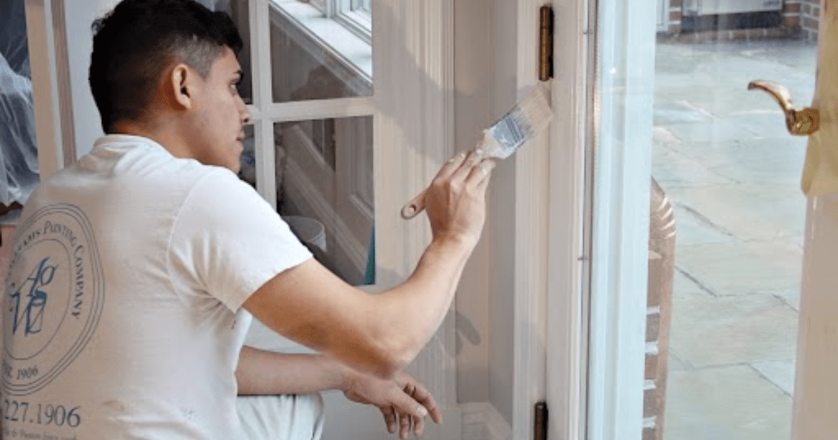 A professional painter in an A.G. Williams Painting Company uniform carefully painting the trim of an interior window with a small brush, ensuring a clean and detailed finish.