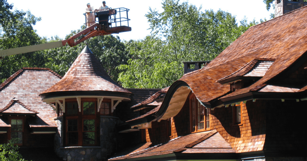 Two painters using a lift to access high areas of a house roof.