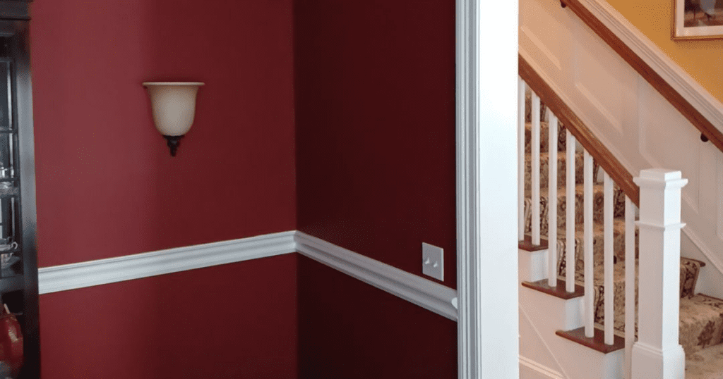 Room with rich red walls and white chair rail molding, leading to a staircase with white spindles and wood railing.