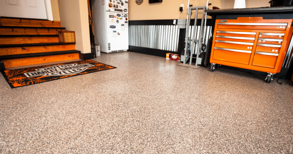Residential garage floor with our concrete floor coatings, featuring wooden stairs, a Harley-Davidson branded mat, and an orange tool chest.