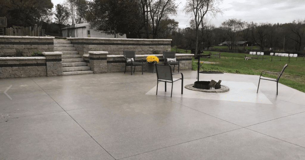 Outdoor concrete patio with a smooth polyaspartic finish, fire pit in the center, and stone retaining wall with steps.