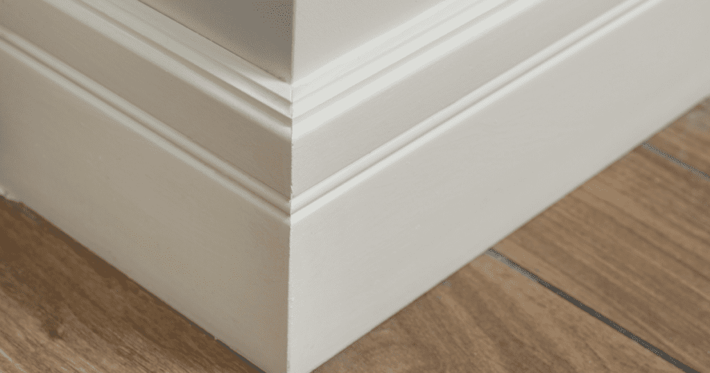 Close-up of a white baseboard with smooth edges and a seamless finish, meeting natural wood flooring.