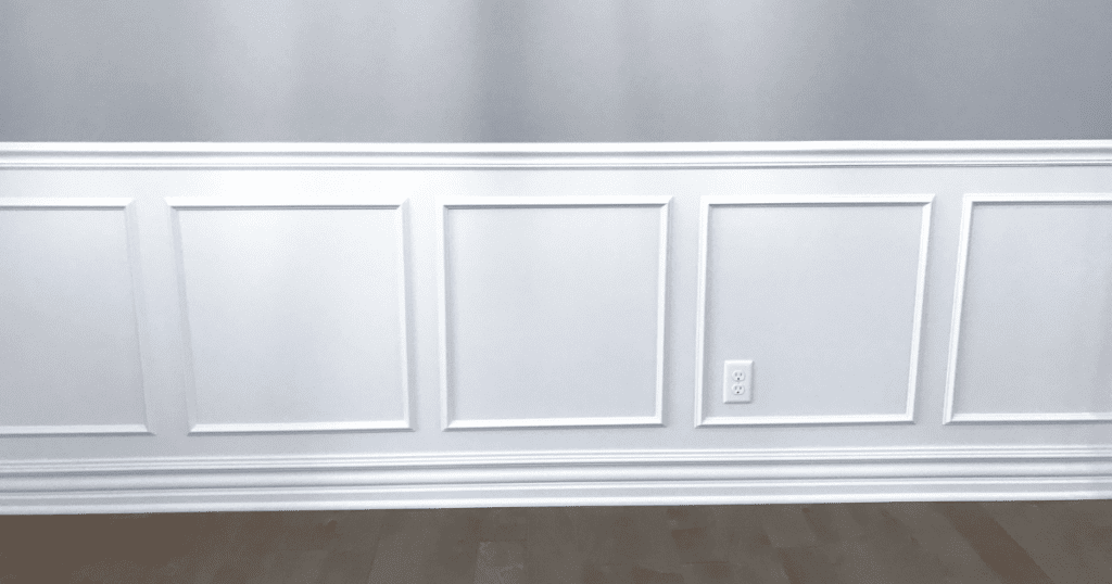 A section of custom white wainscoting with crisp, clean lines and a professional finish against a light gray wall.