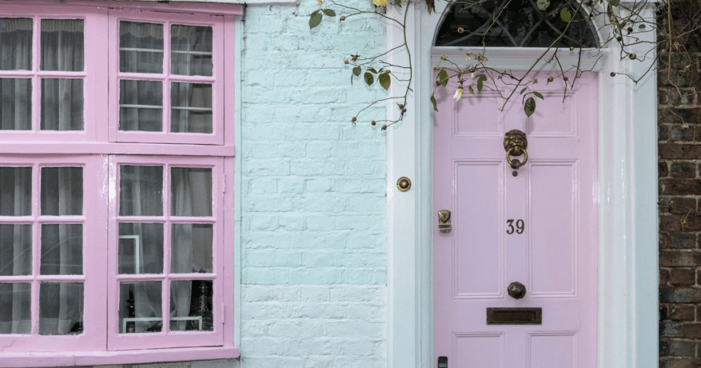 Light pink front door and window frames on a soft mint-green painted brick home.