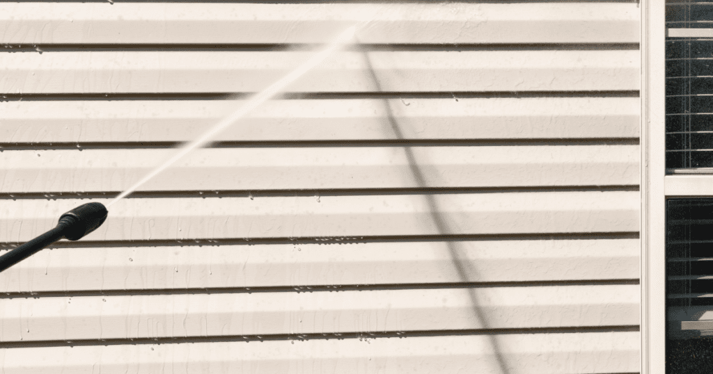 Powerwashing vinyl siding on a home to prepare for painting.