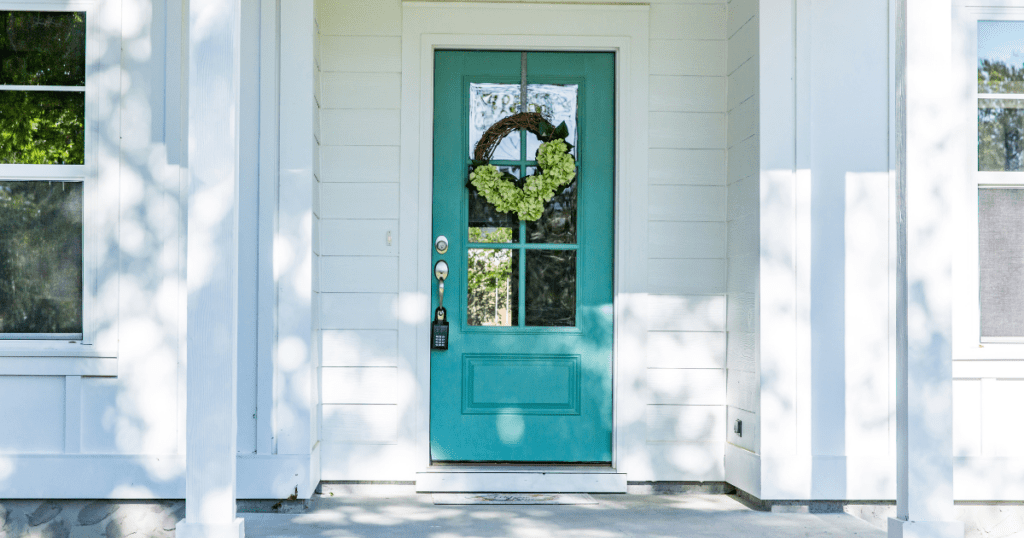 Teal-painted front door with floral wreath on a clean white modern porch.