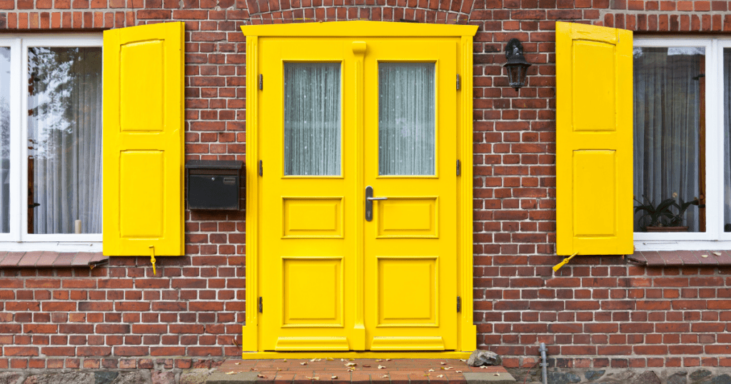 Bright yellow double door and shutters on a classic red brick home exterior.