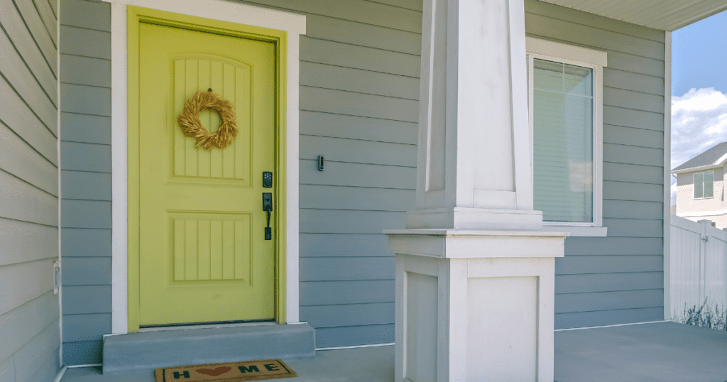 Soft green front door with a wreath on a light gray and white home exterior.