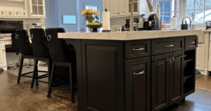Refinished black kitchen island with white quartz countertop and upholstered black barstools.