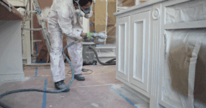 The best home painter using spray equipment to apply finish to cabinet base in a protected work area. Cabinet refinishing is an excellent, low cost way for homeowners to increase home value.