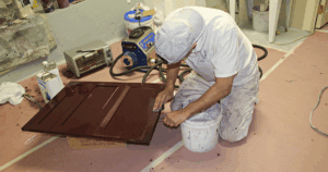 A craftsman from A.G. Williams hand-prepping a burgundy cabinet door.