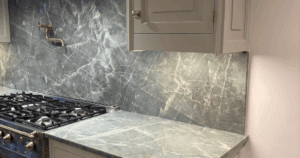 Seamless marble kitchen backsplash and countertop with expertly camouflaged electrical outlet and brass pot filler.