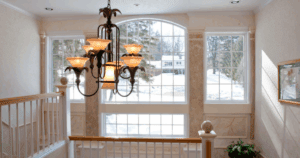 Bright stairwell with large windows, soft beige wallpaper, and a dramatic wrought-iron chandelier.