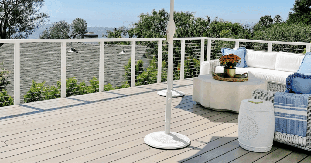 A clean, light-stained deck with white railing, modern furniture, and scenic hillside views.