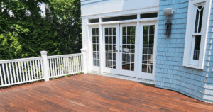 Newly stained hardwood deck with white railing outside a light blue home.