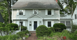 Front of a colonial-style home with muted green siding, white shutters, and landscaped garden.