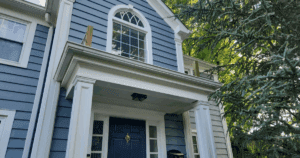 Blue home with crisp white trim and a detailed entry portico featuring columns and an arched window.