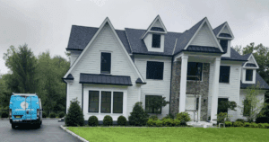 Large modern home with white siding, black window trim, and a prominent stone column, with an A.G. Williams van parked in the driveway.