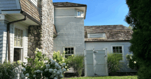 Exterior of a home with light gray shingles, natural stone chimney, and wood roof under clear skies.