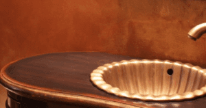 Bronze-toned textured wall with an antique vanity and scalloped sink basin.