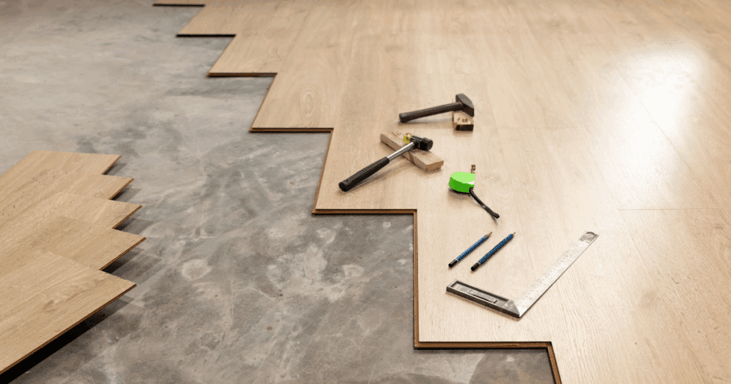 Partially installed hardwood flooring on concrete subfloor with tools laid out.