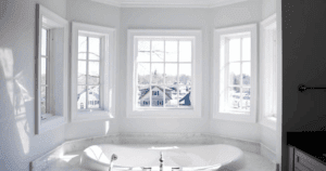Luxurious soaking tub surrounded by white-framed windows and soft gray walls.