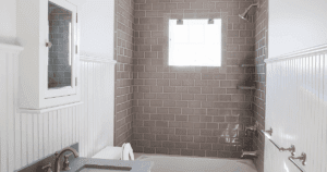 Bathroom with white wainscoting, light gray subway tile shower, and chrome fixtures.