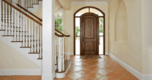 Traditional entryway with cream-colored walls, terracotta floor tiles, and a grand wooden front door.