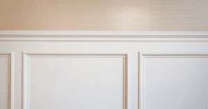 Close-up of white wainscoting and beige grasscloth wall above.