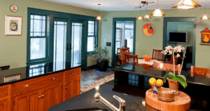 Eclectic kitchen with green walls, teal window trim, black countertops, and warm wood cabinetry.