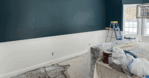 Interior room with a dark teal upper wall, white lower wall, and protective coverings during painting.