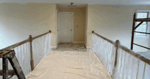 Upper hallway covered with drop cloths and plastic sheeting, prepped for painting.