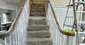 Staircase wrapped in plastic and drop cloths to protect flooring and handrails during painting.