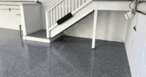 Epoxy-coated garage floor under a stairwell with white railing and base trim.