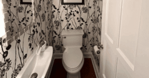 Bold black and white floral wallpaper in a compact powder room with traditional fixtures.