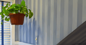 Subtle blue vertical striped wallpaper in a stairwell with a hanging plant and natural light.