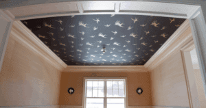 Ceiling covered in dark wallpaper with a white bird pattern, contrasted by neutral-toned walls. For ceiling painting tips, always think outside the box.