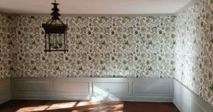 Sunlit dining room with green and blue floral wallpaper above soft gray wainscoting.