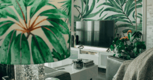 Living room with bold tropical leaf wallpaper behind a TV, surrounded by plants and botanical decor.