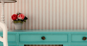 Classic striped wallpaper in soft red and cream tones behind a turquoise console with decorative flowers.
